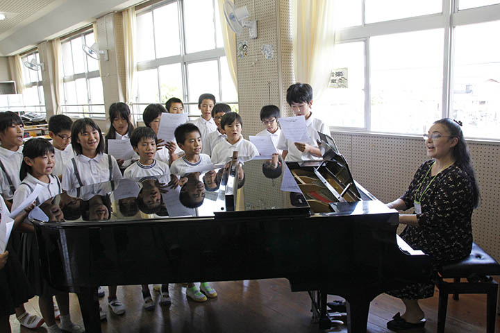 寄贈されたグランドピアノの伴奏にあわせて、歌を歌う児童たち