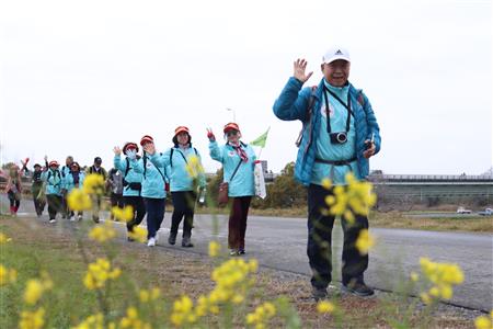 春の訪れを感じさせる菜の花を前に手を振る参加者